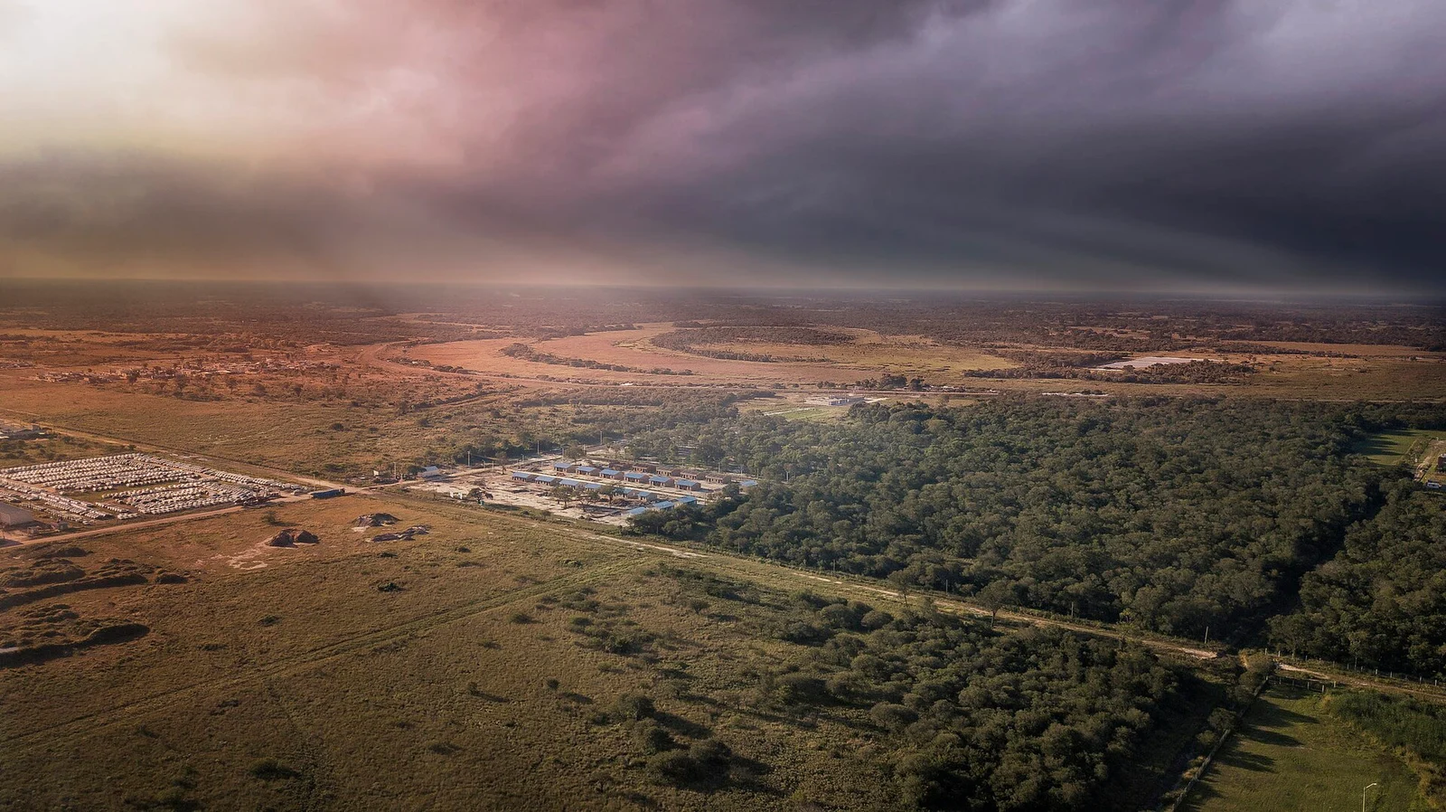 Paisaje rural con campos y un río bajo nubes al atardecer